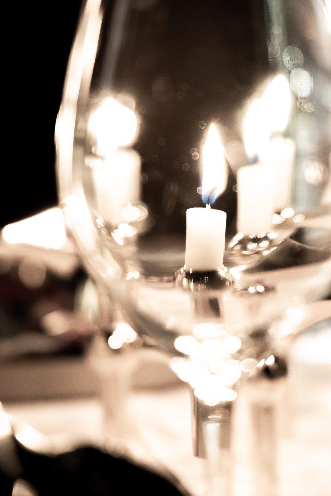 A single candle flame seen through the bowl of a wine glass on a laid table