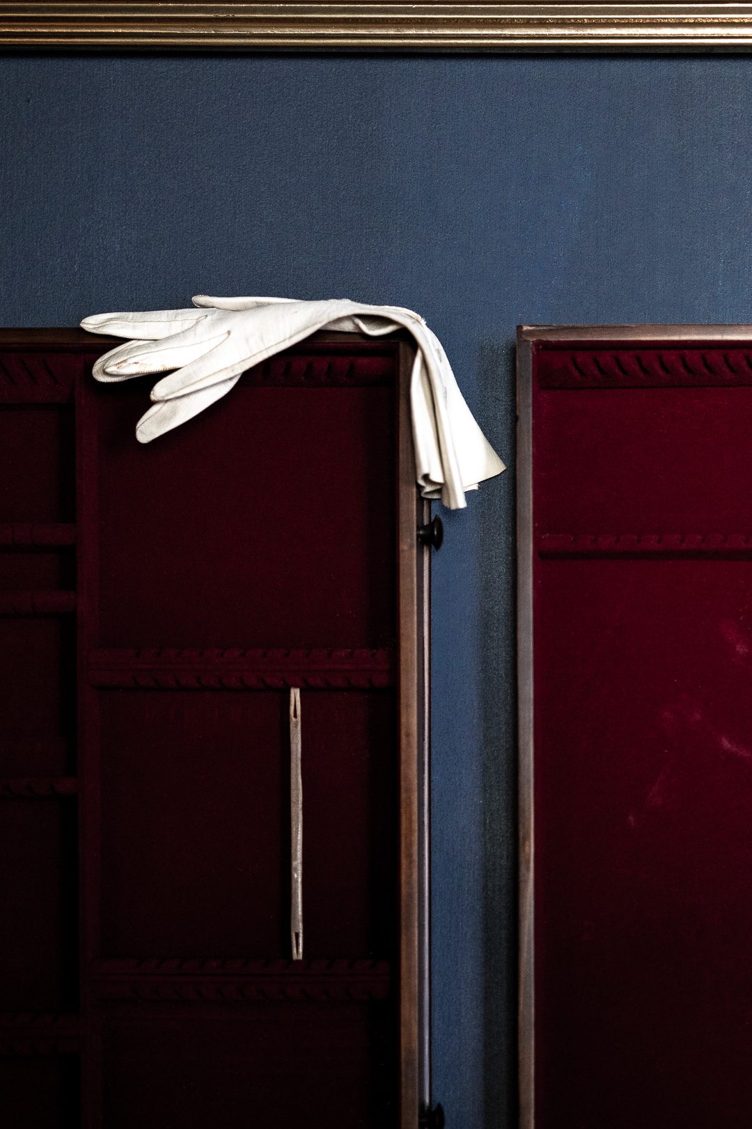 A pair of white gloves left folded over antique cases lined in deep red velvet against a blue wall