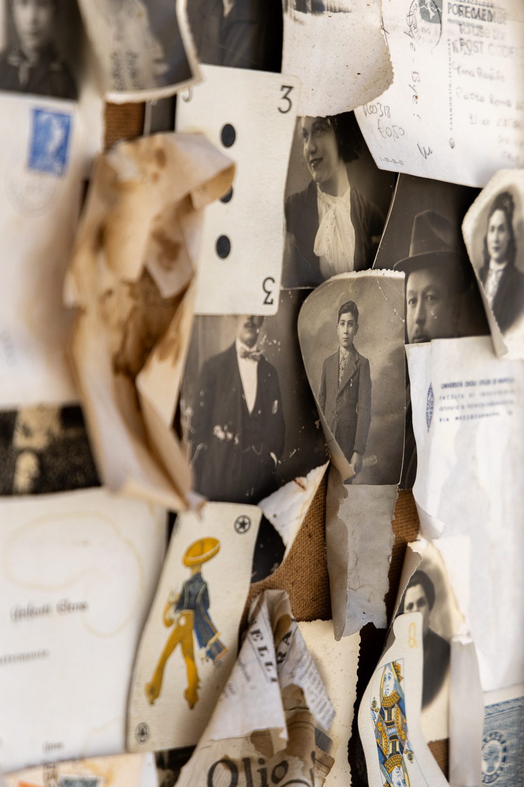 A wall layered with torn vintage photographs, handwritten postcards and old playing cards