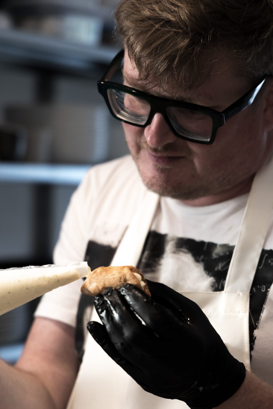 Mikko filling a cannolo shell from a piping bag with a gloved hand in the kitchen