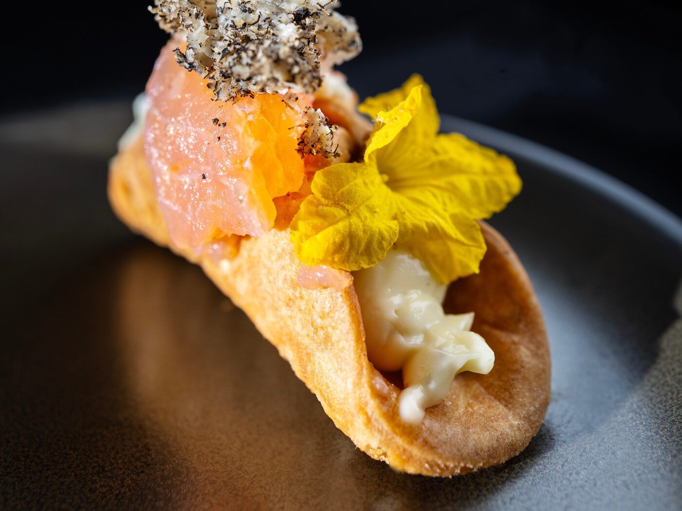 A single crisp shell filled with raw fish, cream, shaved black truffle and a yellow garden flower
