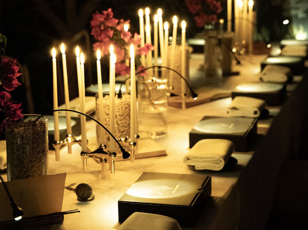 A long candlelit table set with tapers, bougainvillea and a sealed black box at every place