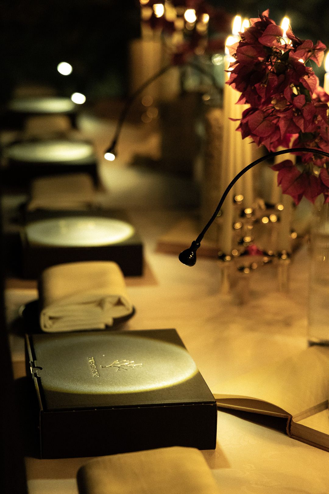A sealed black box embossed with the gold Five Seasons tree, lit by candlelight beside folded linen